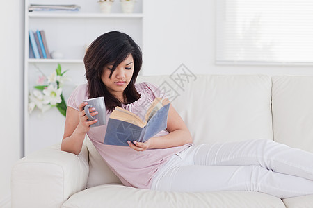 女人躺在沙发上 拿着杯子和书高清图片