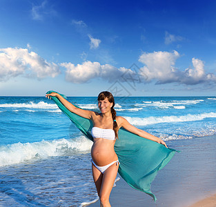 美丽的孕妇在蓝沙滩上行走成人父母海滩海洋母亲婴儿母性家庭支撑泳装图片