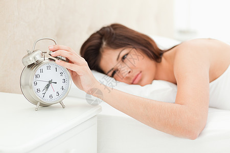 一个女人躺在床上 手放在闹钟上图片