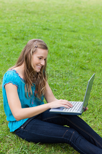 年轻笑笑的女孩在她笔记本电脑上打字时坐着图片