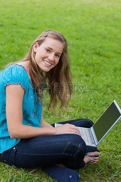 年轻微笑的女孩在使用笔记本电脑时看着相机图片