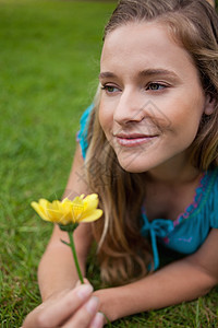 年轻有思想的女孩躺在草地上 拿着花朵图片