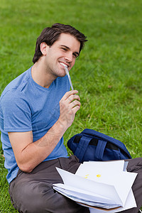 坐在草地上工作时微笑的年轻男人图片