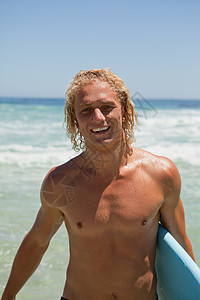 微笑的人站在水中 拿着冲浪板站着图片