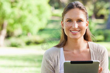 带着平板电脑坐在草坪上的笑女人图片