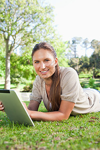 带着平板电脑躺在草地上的笑容女人图片