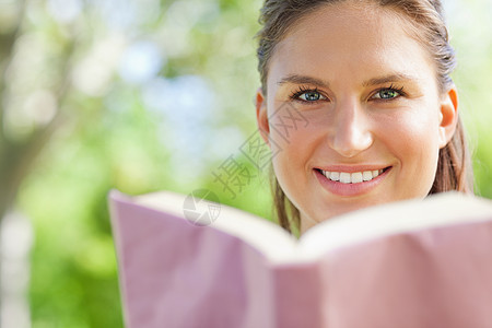 微笑的女人在公园里看书女性阅读小说绿色外表自由阳光喜悦闲暇树叶图片