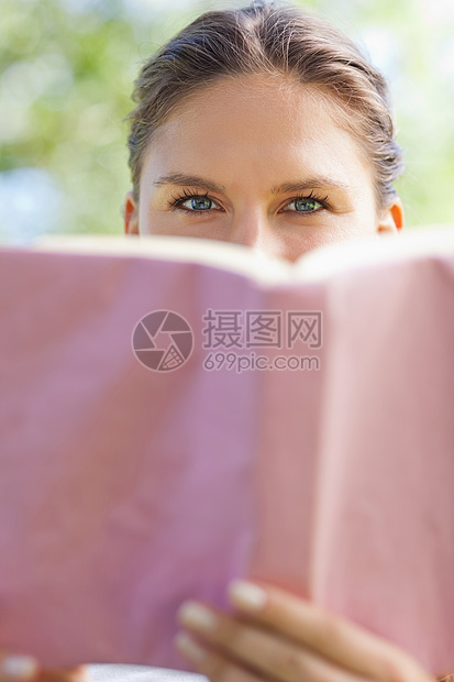女人把脸藏在公园里一本书后面图片