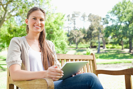 带着平板电脑在公园的长椅上微笑的女人图片