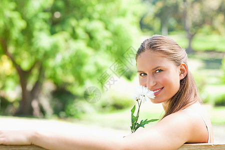 一个微笑的女人的侧面 闻着一朵花的香味图片