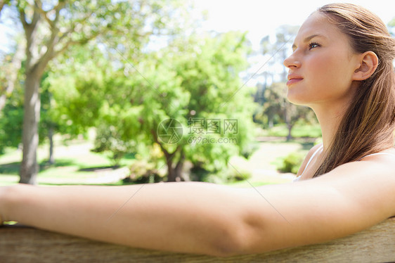 坐在公园长椅上的女人的侧面视图闲暇女性草地自由阳光树叶喜悦绿色外表森林图片