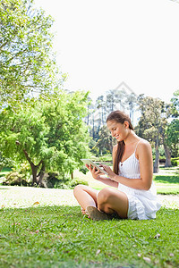 一个带着平板电脑的 躺在草坪上微笑着的女人的侧面景色图片