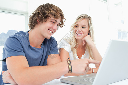 一对微笑的夫妇看着笔记本电脑 女人看着快乐外表女性成年人金发女郎年轻人桌子图片