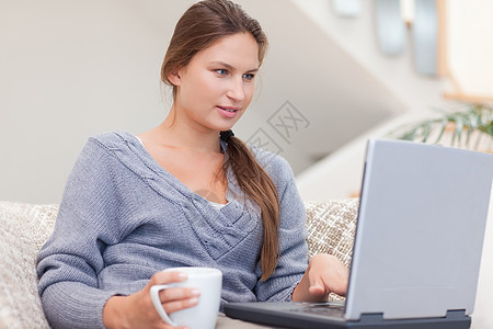 妇女在喝咖啡时使用笔记本电脑闲暇乐趣房子长椅快乐幸福女性沙发网络互联网图片
