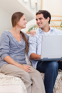 一对用笔记本电脑微笑的情侣的肖像妻子沙发网络夫妻长椅技术拥抱年轻人闲暇沟通图片