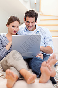 躺在沙发上时使用笔记本电脑的一对夫妇肖像技术上网微笑冲浪快乐夫妻网络妻子拥抱已婚图片