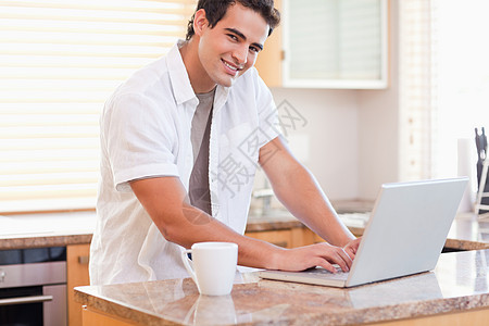 男性在厨房的笔记本电脑上工作图片