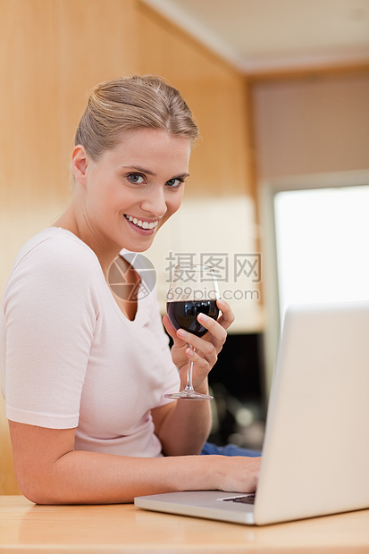 一个女人在喝红酒时使用笔记本电脑的肖像图片