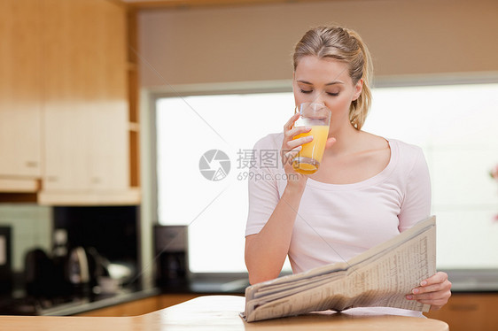 年青女子在喝橙汁时看新闻图片