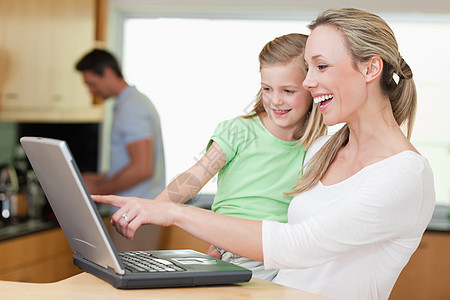 快乐的母亲和女儿使用笔记本电脑与父亲在背面图片
