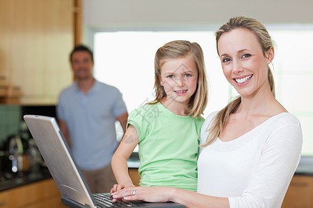 母亲和女儿与父亲一起使用笔记本电脑的背景情况图片