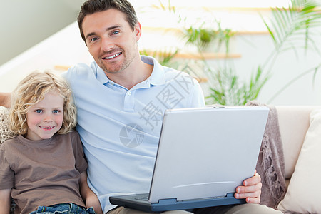 父亲和儿子用笔记本电脑坐在沙发上图片