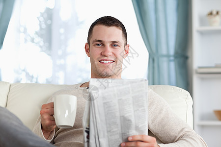 年轻人在看新闻时喝茶房间白色阅读沙发生活微笑长椅报纸闲暇饮料图片