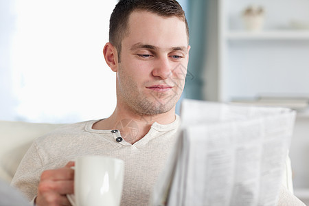 笑脸男人在看新闻时喝咖啡白色沙发闲暇报纸阅读生活年轻人住房长椅饮料图片