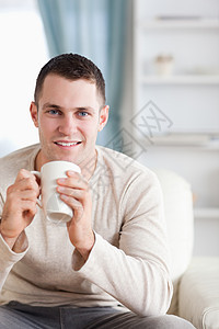 男人喝咖啡的肖像微笑牛奶杯子外表年轻人电视享受咖啡饮料沙发图片