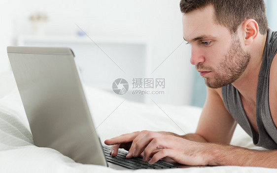严重男人躺在肚子上时使用笔记本电脑图片