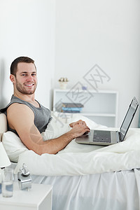 使用笔记本电脑微笑的男人的肖像网络快乐技术乐趣互联网工作闲暇卧室睡衣冲浪图片