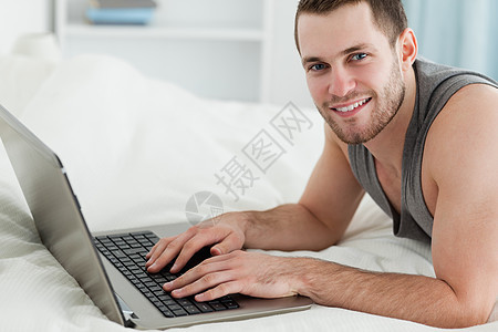 英俊男人躺在肚子上时用笔记本电脑图片
