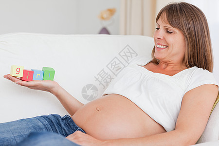 美丽的孕妇在玩木木砖和有t的游戏沙发女士女孩玩具喜悦腹部生活母亲情感长椅图片