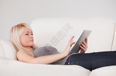 漂亮的女人躺在沙发上 在平板计算线上放松图片