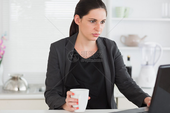 女人在看笔记本电脑时拿着杯子图片