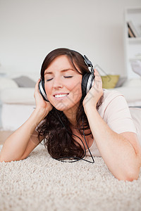 黑褐色快乐女人躺在地毯上时使用耳机图片