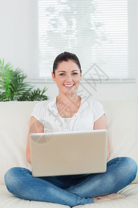 微笑的女人用笔记本电脑坐在沙发上图片