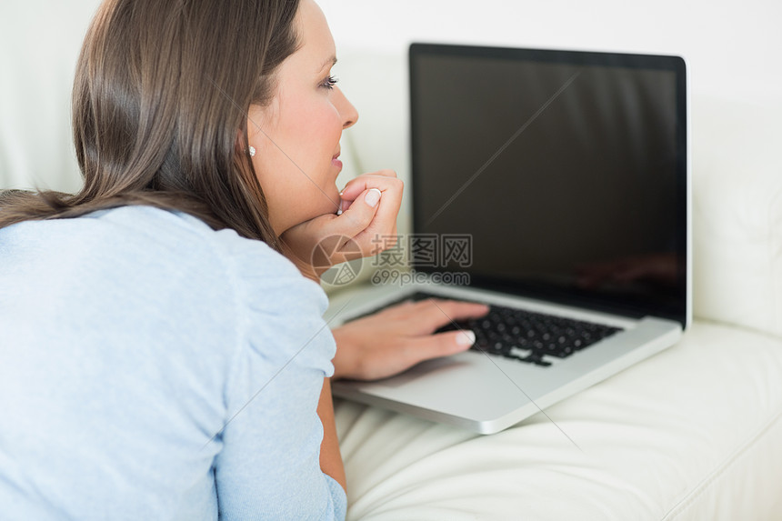 妇女用笔记本电脑打字客厅公寓长椅住所家庭女性技术棕色头发女士图片