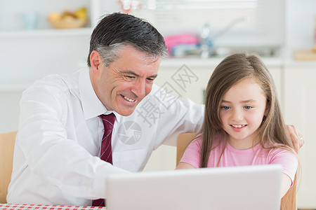 男人和女孩用笔记本电脑坐在厨房图片