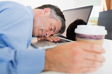 男人一边喝咖啡一边睡在笔记本电脑上衬衫睡眠套装头发生意人桌子技术管理人员领带商务图片