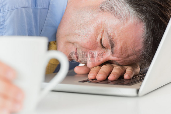 商务人士在喝咖啡时睡在笔记本电脑上图片