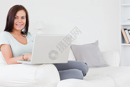 坐在沙发上 使用笔记本电脑的迷人黑发美女图片