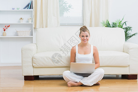 微笑的女人坐在地板上时拿着笔记本电脑图片