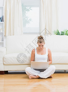 妇女坐在地板上时用笔记本电脑打字图片