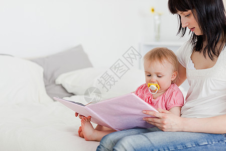 漂亮的黑褐色女人 在她坐着时给孩子看一本书图片