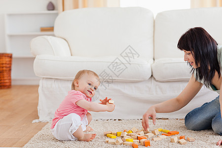 可爱的女人坐在地毯上与婴儿玩耍 而她却坐在地毯上图片