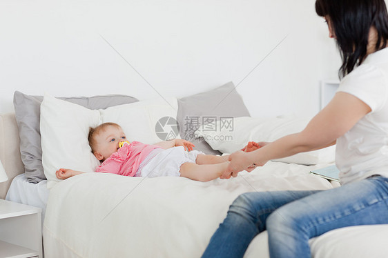 可爱的黑褐色女人坐在床上与婴儿玩耍图片