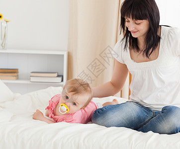 可爱的黑褐色女人看着她躺在床上的婴儿图片
