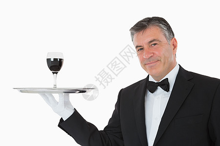 在银盘上拿着一杯酒的笑脸服务员套装领结服务衬衫白色玻璃平衡男性奢华头发图片