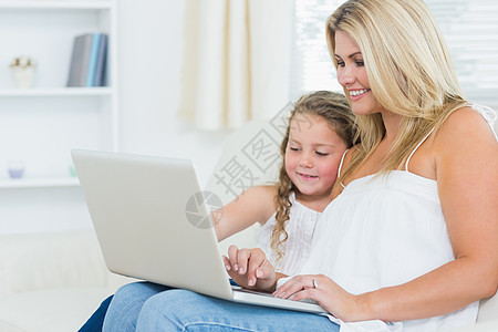在笔记本电脑上微笑的母亲和女儿图片